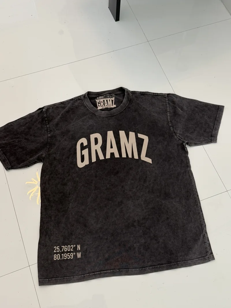 Front of the washed charcoal GRAMZ Arch Tee laid flat, showing the arched GRAMZ chest print and Miami coordinates at the hem