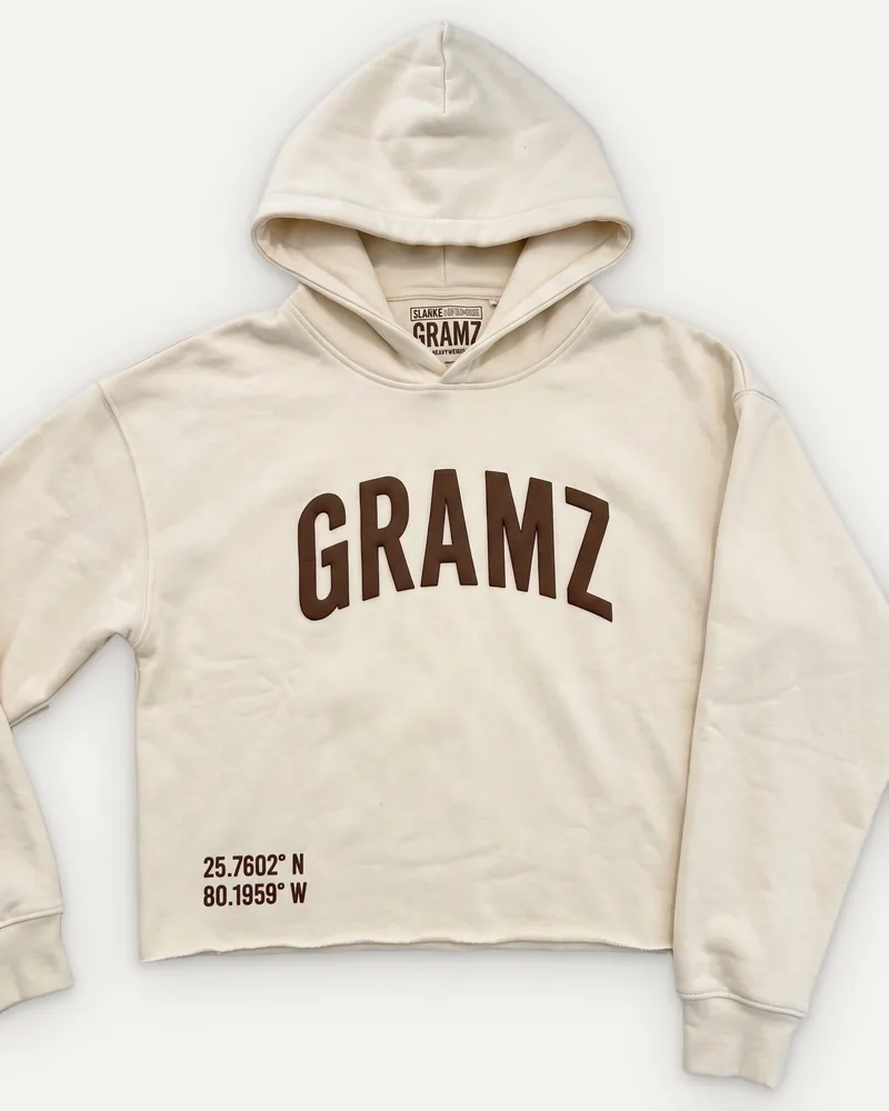 Design rendering: cream cropped hoodie with a brown arched GRAMZ chest print and Miami coordinates at the hem