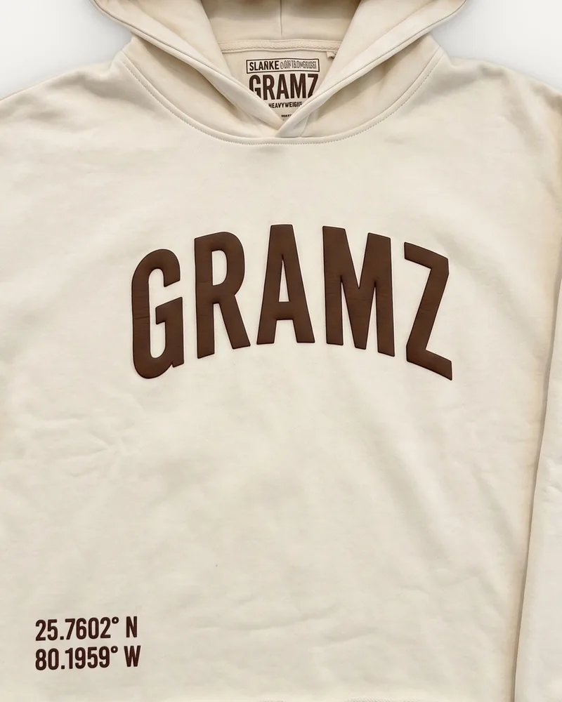 Design rendering: close-up of the brown arched GRAMZ chest print and Miami coordinates on the cream cropped hoodie
